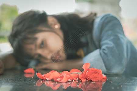 有选择地关注红玫瑰花瓣 寂寞的年轻少年沉浸在桌子上 头低下——爱情破裂或心碎的概念 (笑声)图片