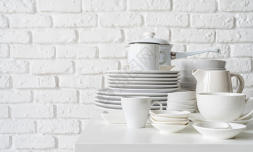 白砖墙底桌边的白陶瓷盘和餐具堆叠件平底锅陶瓷咖啡店刀具盘子用具陶器烹饪制品杯子图片