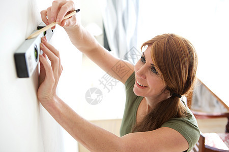 妇女用精神水平和铅笔在墙上作标记图片