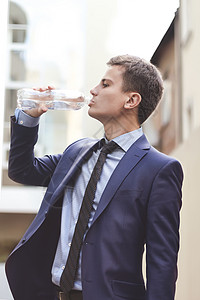 有西装的商务人士拿着水瓶 在户外喝酒 年轻的商务人士喝着城里的清水 (笑声)图片