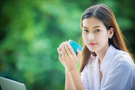 一位亚洲女性拿着咖啡杯喝水 早上在家使用笔记本电脑工作图片