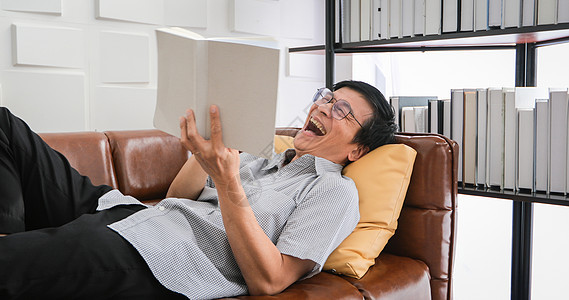 亚洲老人看书 在家客厅沙发上笑亚洲老人肖像在家阅读杂志是放松和快乐图片