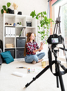 一位女士使用安装在三脚架上的数码相机为她的艺术博客制作视频手势商业艺术家画家相机女孩教学刷子工艺训练图片