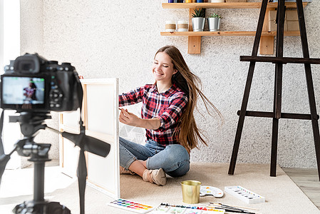 一位女士使用安装在三脚架上的数码相机为她的艺术博客制作视频画家技术水彩商业女孩爱好教程训练绘画教育图片
