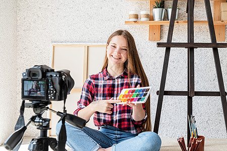 一位女士使用安装在三脚架上的数码相机为她的艺术博客制作视频爱好青少年教育相机技术画家播送刷子工作教学图片
