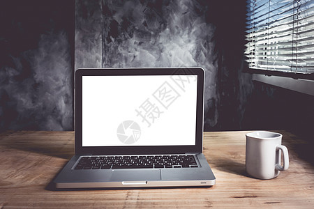 手持白色空白屏幕的笔记本电脑和木制桌子上的咖啡杯 有墙壁背景装饰咖啡房间监视器工作展示风格办公室杯子技术图片