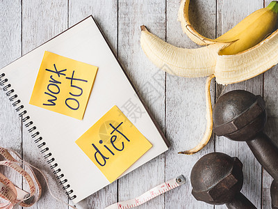 香蕉加铁哑铃 测量磁带和木制桌底的笔记本 锻炼和饮食概念图片