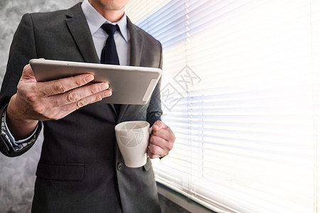 近距离靠近商务人士使用平板电脑和咖啡杯 站在办公室的窗户边站着图片