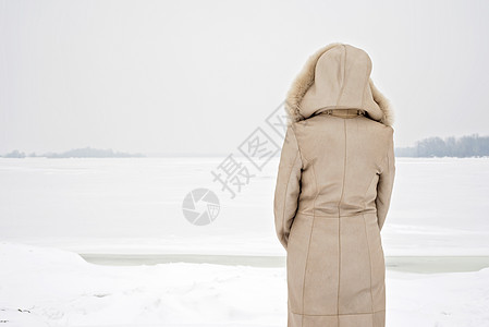 女人靠近冬季的冷冻河女士兜帽成人沉思树木中年女性头发外套薄片图片