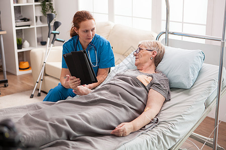 使用平板电脑护理院的女医生老年助手祖母药片拐杖技术退休病人女士微笑图片