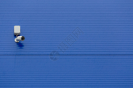 大型蓝色钢筒墙上的小型白色安全摄像头建造控制板财产警卫电子控制监视技术危险记录图片