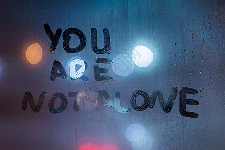 “你并不孤单”这句话是用手指在夜间湿玻璃上写的 背景中有模糊的经典蓝灯图片