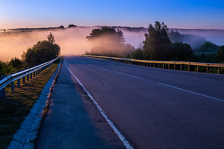 清晨在河附近的夏季高速公路上用防守铁轨吹起的浓雾沥青栏杆薄雾森林路线旅游运输护栏风景障碍图片