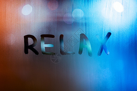 “放松”这个词是用手指在湿玻璃上写的 背景灯光模糊图片