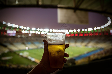 啤酒可处理的玻璃杯 背景是足球体育场图片