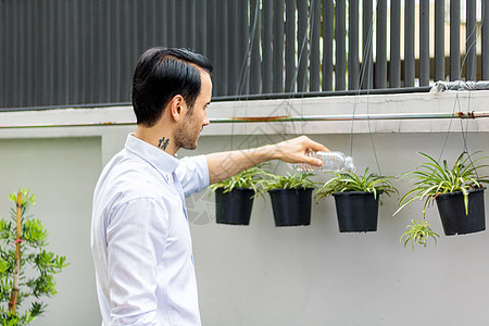 年轻人用可回收塑料瓶在盆栽植物中浇水 在给植物浇水时 他扭动塑料瓶进行回收 在花园里工作的年轻人男人学习衬衫技术闲暇男性公园互联图片