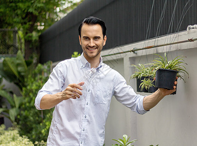 年轻人用可回收塑料瓶在盆栽植物中浇水 在给植物浇水时 他扭动塑料瓶进行回收 在花园里工作的年轻人电脑学习商业咖啡报纸教育学生笔记图片