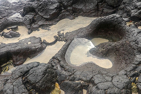 底部有白色沙子的岩石凹陷处充满了海水 在印度洋海岸巴厘岛印度尼西亚的熔岩床中挖掘出的小池塘 潮水在黑色岩石中挖出了小湖热带火山岩图片