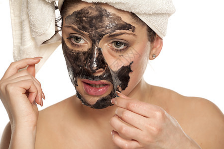 女人脱下她脸上的黑面罩木炭女士皮肤黑色温泉化妆品治疗女孩产品毛巾图片