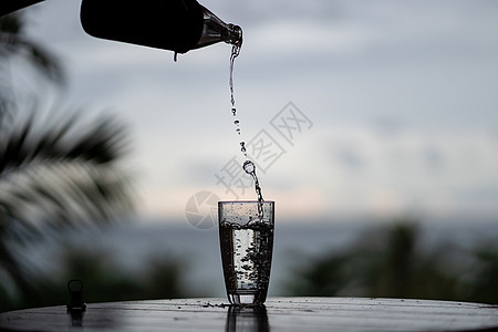 从玻璃杯中瓶瓶子里浇水到自然的后院反射水晶液体背景生活手指桌子飞溅玻璃矿物图片