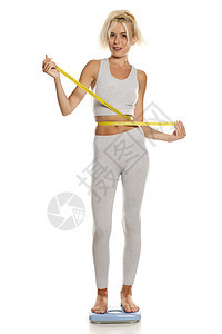 身着灰色腿部的瘦弱运动健壮年轻女子站在一个比例尺上健身房数字腰部运动装女孩绑腿衣服女士衬衫女性图片