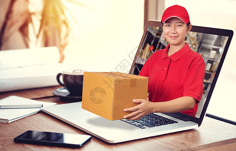 身穿红色衬衫 仓库背景模糊的亚洲送货员 拿着包裹里的货物订单 从笔记本电脑里拿出来 在线订购和送货服务理念图片