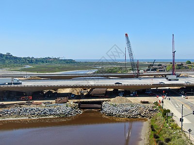 在小河上建造高速公路桥梁的空中观察图景职业鸟瞰图卡车承包商交通电缆起重机运输技术工人图片