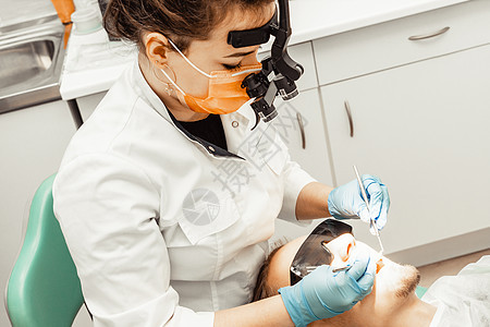 牙医年轻女人对待病人的男人 医生使用一次性手套 口罩和帽子 牙医在病人的嘴里工作 使用专业工具访问口服卫生女士牙疼女性牙齿矫正卫图片