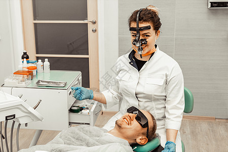 牙医年轻女人对待病人的男人 医生使用一次性手套 口罩和帽子 牙医在病人的嘴里工作 使用专业工具牙疼诊所假牙程序访问女士药品牙齿镜图片