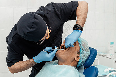 一位年轻的男牙医在治疗病人 牙科 外科的医疗操作 牙医的专业制服和设备 医疗保健装备医生工作场所 牙科假牙卫生工具女性医学牙齿药图片