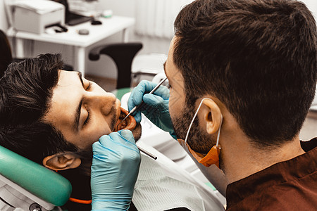 一位年轻的男牙医在治疗病人 牙科 外科的医疗操作 牙医的专业制服和设备 医疗保健装备医生工作场所 牙科矫正医院牙科技师女性镜子微图片