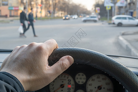 从车上看 男人的手放在汽车的方向盘上 位于人行横道和过马路的行人对面图片