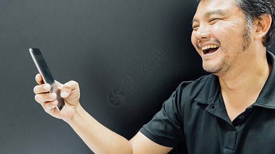 亚洲男人在深色风格中使用智能手机微笑旅行头发黑色情感乐趣成人快乐技术男性马球图片