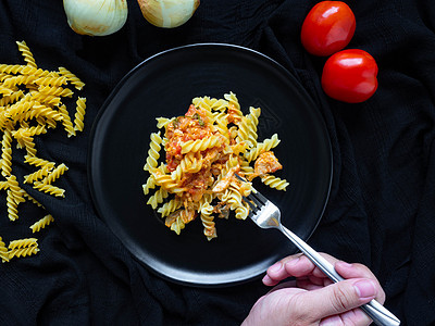 Fusilli 番茄酱鸡 配料西红柿 鸡肉 大蒜 胡椒 洋葱 是放在黑盘黑色织物背景上的意大利食物美食香料食谱猪肉蔬菜海洋面条沙图片