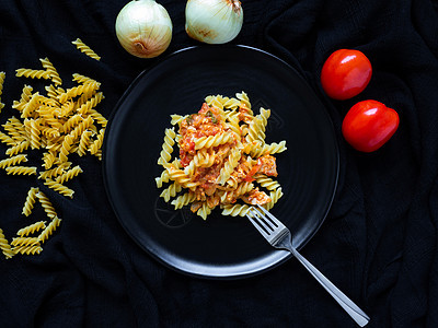 Fusilli 番茄酱鸡 配料西红柿 鸡肉 大蒜 胡椒 洋葱 是放在黑盘黑色织物背景上的意大利食物餐厅盘子面条蔬菜美食香料猪肉午图片