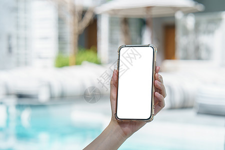 在游泳附近手持空白白屏幕移动电话的妇女 使用在游泳附近的阅读技术水池小样白色社会女性手机展示旅行图片