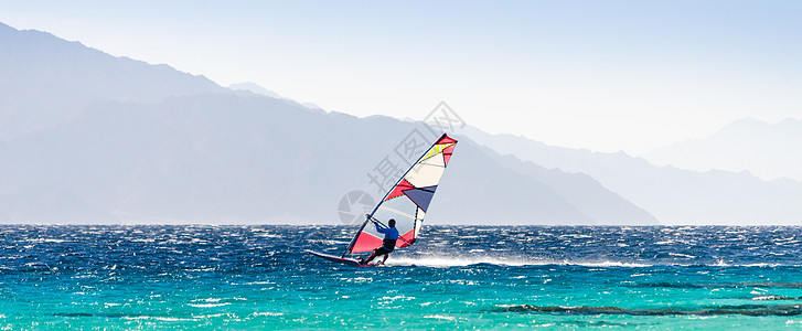 红海的冲浪骑马 在岩石海岸的背景上运动员高山风帆海景极限蓝色地平线热带天空季节图片