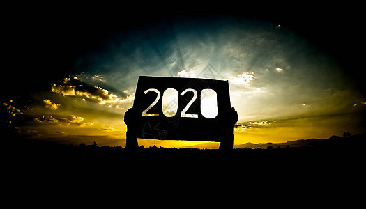 手持回收纸板的剪影 上面有 2020 年的文字 覆盖着日落的天空背景 阳光透过文字闪耀 新年和庆祝的概念图片