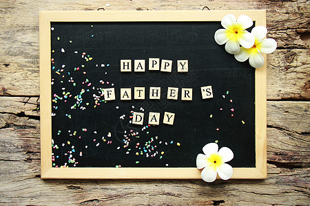 父亲从黑色粉笔板上的木块小地方传来快乐的一天话 用木本底热带花朵装饰图片