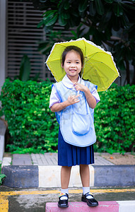 穿着泰国校服 雨伞带黄色雨伞的小女孩幼儿园女孩公园树木学生喜悦下雨教育学校女性图片
