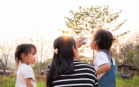亚洲小女孩厌倦了与母亲和姐姐一起在花园玩耍 晚上看着日落 然后喝瓶装水中的自来水孩子们乐趣女孩朋友们家庭女性快乐微笑女儿食物图片