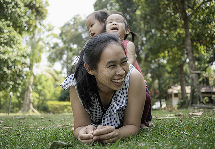 亚洲快乐的年轻母亲躺在草地上 女儿坐在公园后背上图片
