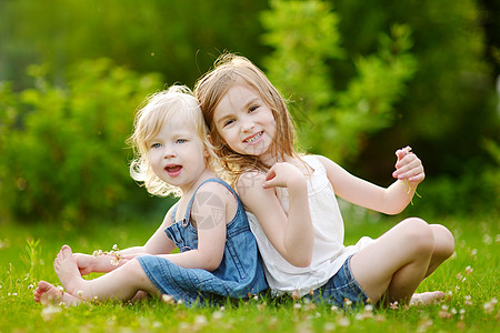 坐在草地上的两个可爱的小妹妹幼儿园微笑喜悦乐趣闲暇孩子们孩子女孩姐姐兄弟图片