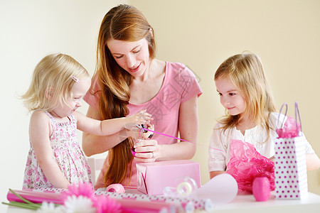 母亲和两个女儿在包着礼物展示孩子父亲纪念日假期圣诞礼物盒子丝带姐姐花朵图片