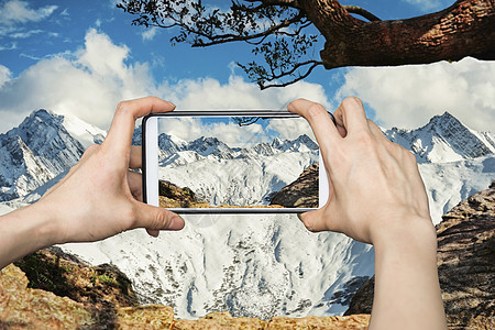 女孩在高雪山的移动智能手机上拍摄照片图片