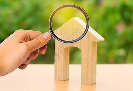 放大镜看着一个有大门口的房子的木制人物 家 负担得起的住房 住宅楼 购买或出售房地产 租金 投资和建筑的概念图片