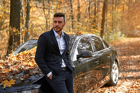 一个英俊的白人年轻男子 穿着商业西装站在黑色汽车附近 在自然界图片