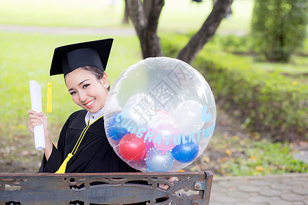 穿着学术服和学校服装的年轻快乐女毕业生肖像长袍文凭召集幸福证书气球学生教育成功研究生图片
