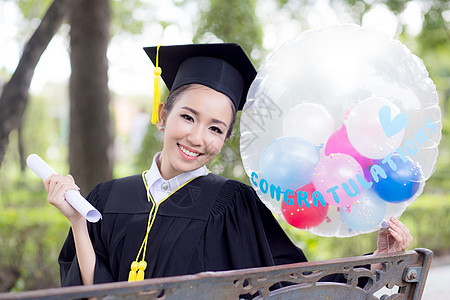 穿着学术服和学校服装的年轻快乐女毕业生肖像学习女孩研究生气球学士文凭召集帽子证书长袍图片