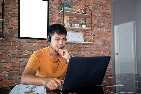 亚洲商务人士正在使用笔记本电脑 并穿戴耳机在网上开会和在家工作时使用耳机人士娱乐男人服务商业网络成人互联网操作员学习图片